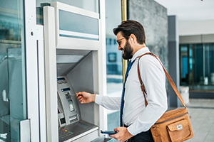 Smiling man wearing sunglasses using a through-the-wall ATM serviced by a top NCR dealer in NJ