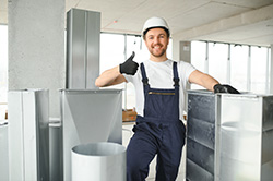 Duct service in Ocean County technician standing among different size and shaped ducts giving a thumbs up.